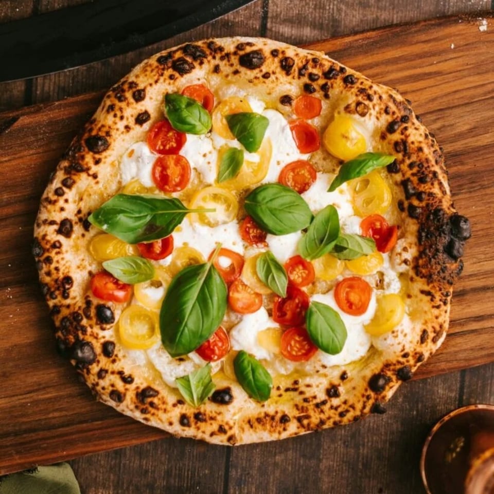 Neapolitan pizza with fresh mozzarella, red and yellow cherry tomatoes, and basil on a wooden board.