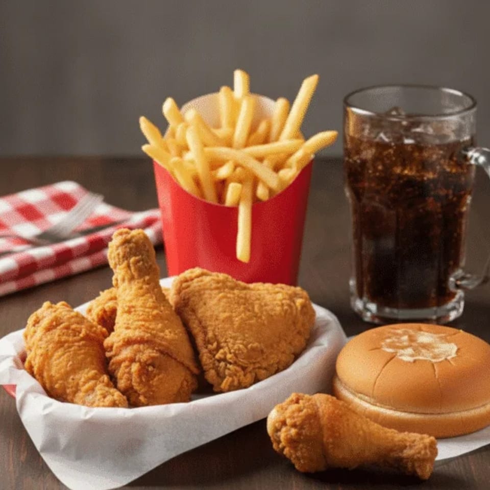 Fried chicken pieces, french fries in a red container, a soda, and a bun on a wooden table.